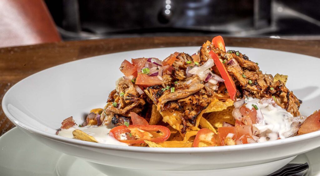 Pulled pork nachos smothered in smoky BBQ sauce, garlic aioli melted cheddar and topped with Pico de Gallo