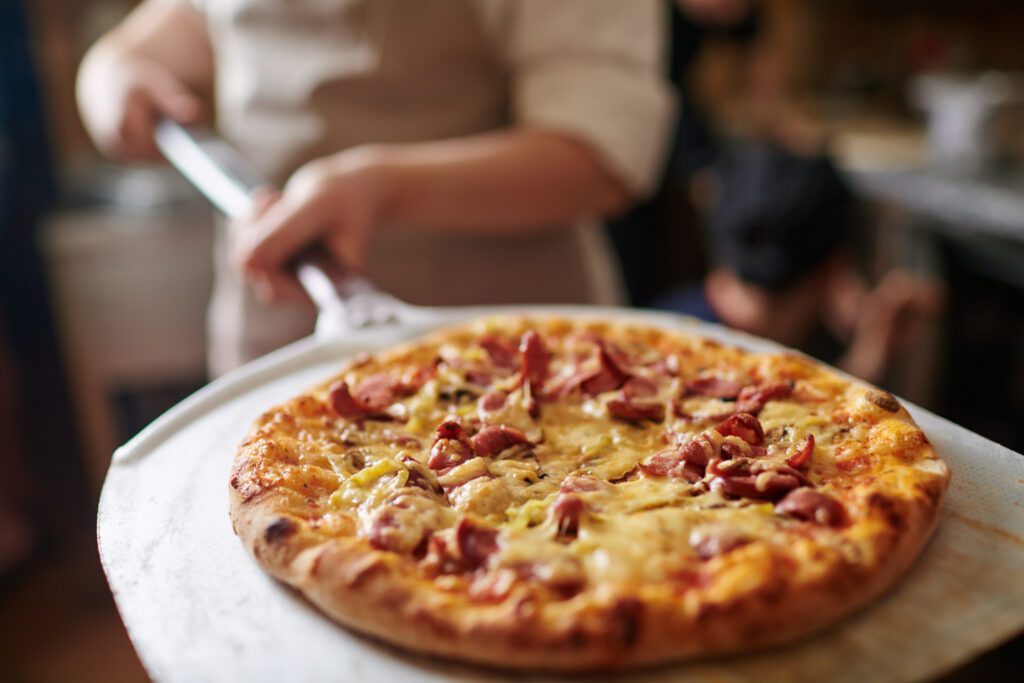 Cook putting out baked pizza from oven